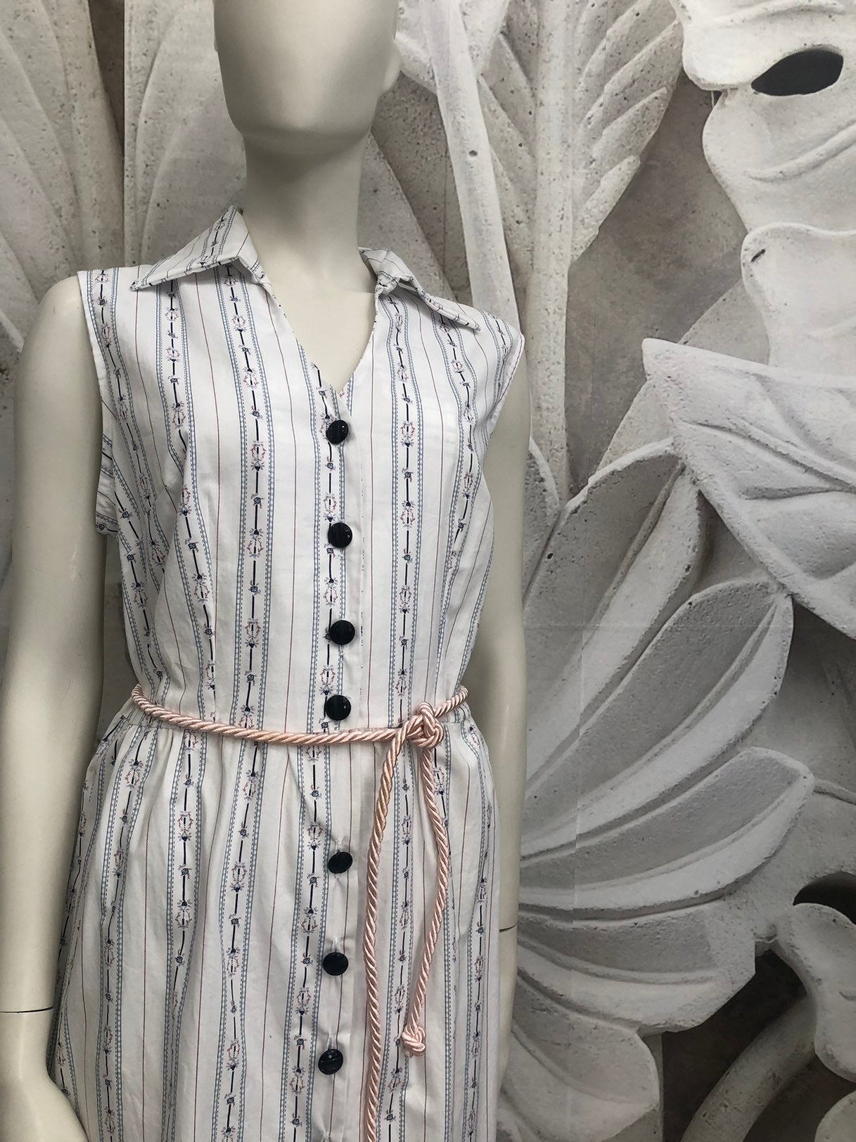 Abito rita in freschissimo cotone bianco con piccoli disegni floreali blu e rosa. Allacciatura davanti con bottoni blu. Cintura in corda di raso rosa