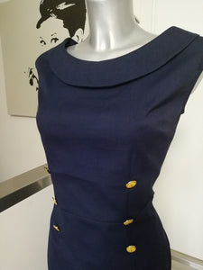 DETTAGLIO DEL CORPINO DAVANTI SMANICATO CON SCOLLO A BARCA, BORDATO DA UN COLLO. BOTTONI DI ABBELLIMENTO METALLO COLOR ORO E SMALTATO GIALLO  CON ANCORA DISEGNATA. TESSUTO IN COTONE A  COSTINA BLU